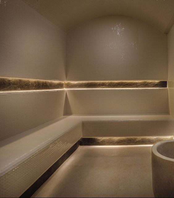 Un hammam marocain élégant aux murs texturés, doté de bancs en marbre blanc, d’un éclairage ambiant chaleureux et d’une décoration raffinée. Une ambiance relaxante parfaite pour une expérience de détente authentique.