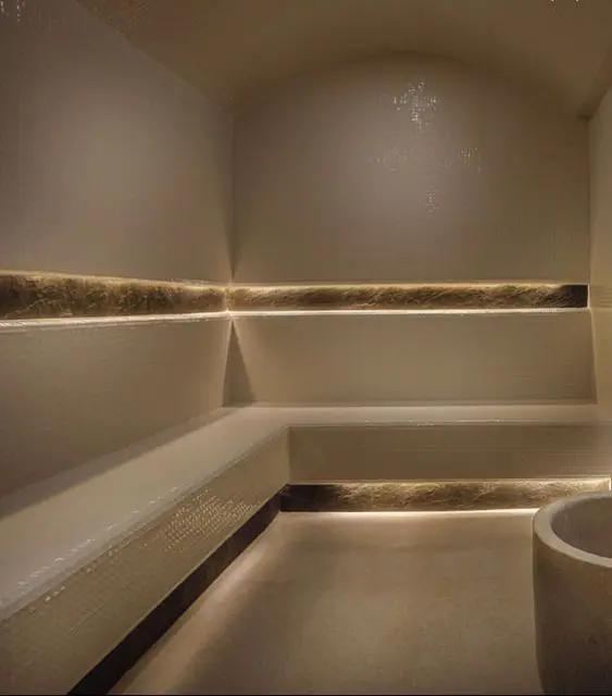 Un hammam marocain élégant aux murs texturés, doté de bancs en marbre blanc, d’un éclairage ambiant chaleureux et d’une décoration raffinée. Une ambiance relaxante parfaite pour une expérience de détente authentique.