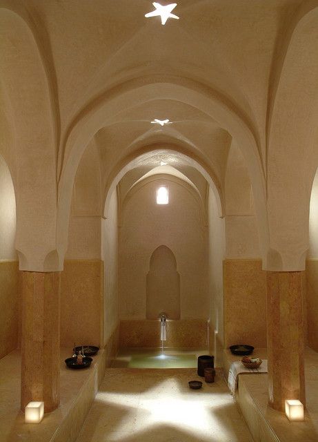 Un hammam marocain traditionnel aux voûtes arquées, doté d’un bassin central en marbre, de colonnes décoratives et d’une lumière naturelle filtrée par des ouvertures au plafond