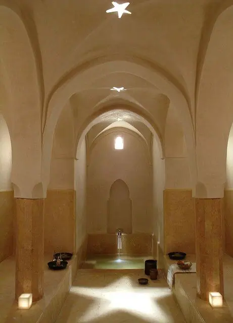 Un hammam marocain traditionnel aux voûtes arquées, doté d’un bassin central en marbre, de colonnes décoratives et d’une lumière naturelle filtrée par des ouvertures au plafond