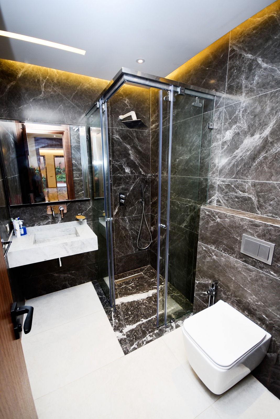 Salle de bain moderne aux murs en marbre noir veiné, dotée d’une douche à porte coulissante en verre transparent, d’un meuble sous vasque blanc et d’un WC suspendu
