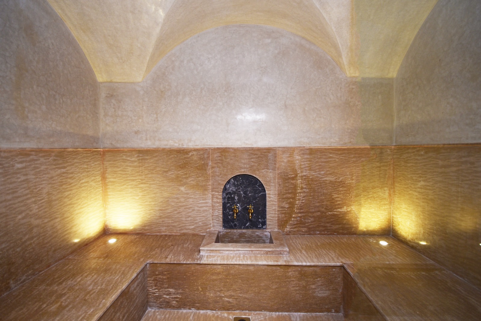 tas (taffadna) murale intégrée dans un hammam marocain, conçue avec des matériaux nobles comme le marbre noir et les robinets dorés, offrant une expérience de détente raffinée.
