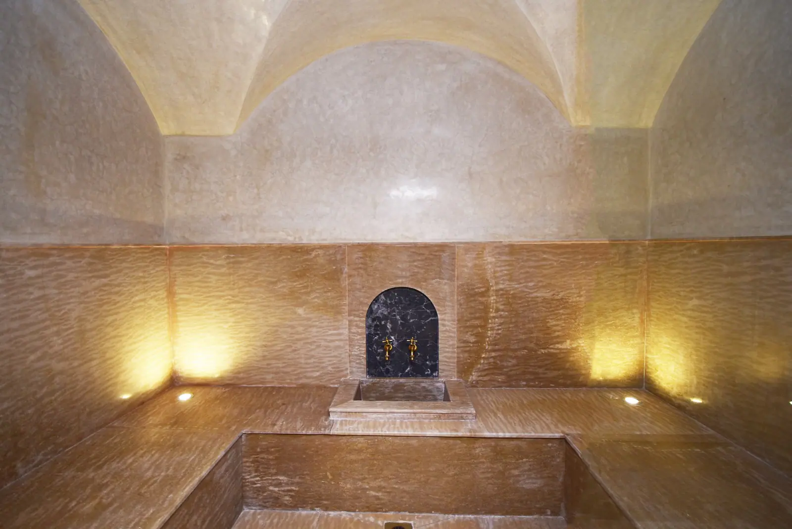 tas (taffadna) murale intégrée dans un hammam marocain, conçue avec des matériaux nobles comme le marbre noir et les robinets dorés, offrant une expérience de détente raffinée.