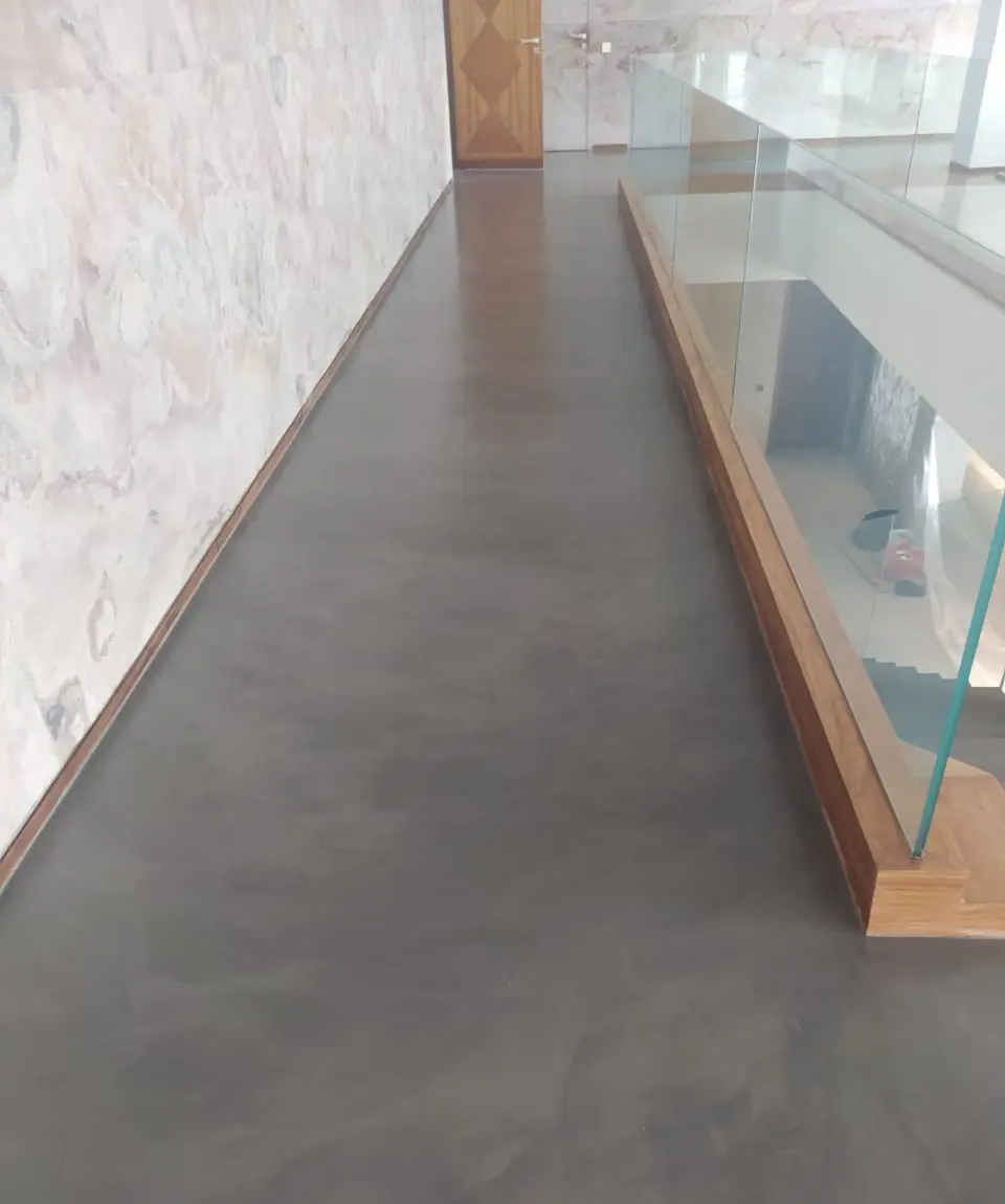 "Un corridor contemporain aux murs en marbre veiné, doté d’un sol en béton ciré gris foncé et d’une balustrade en verre transparent pour une ambiance lumineuse et élégante