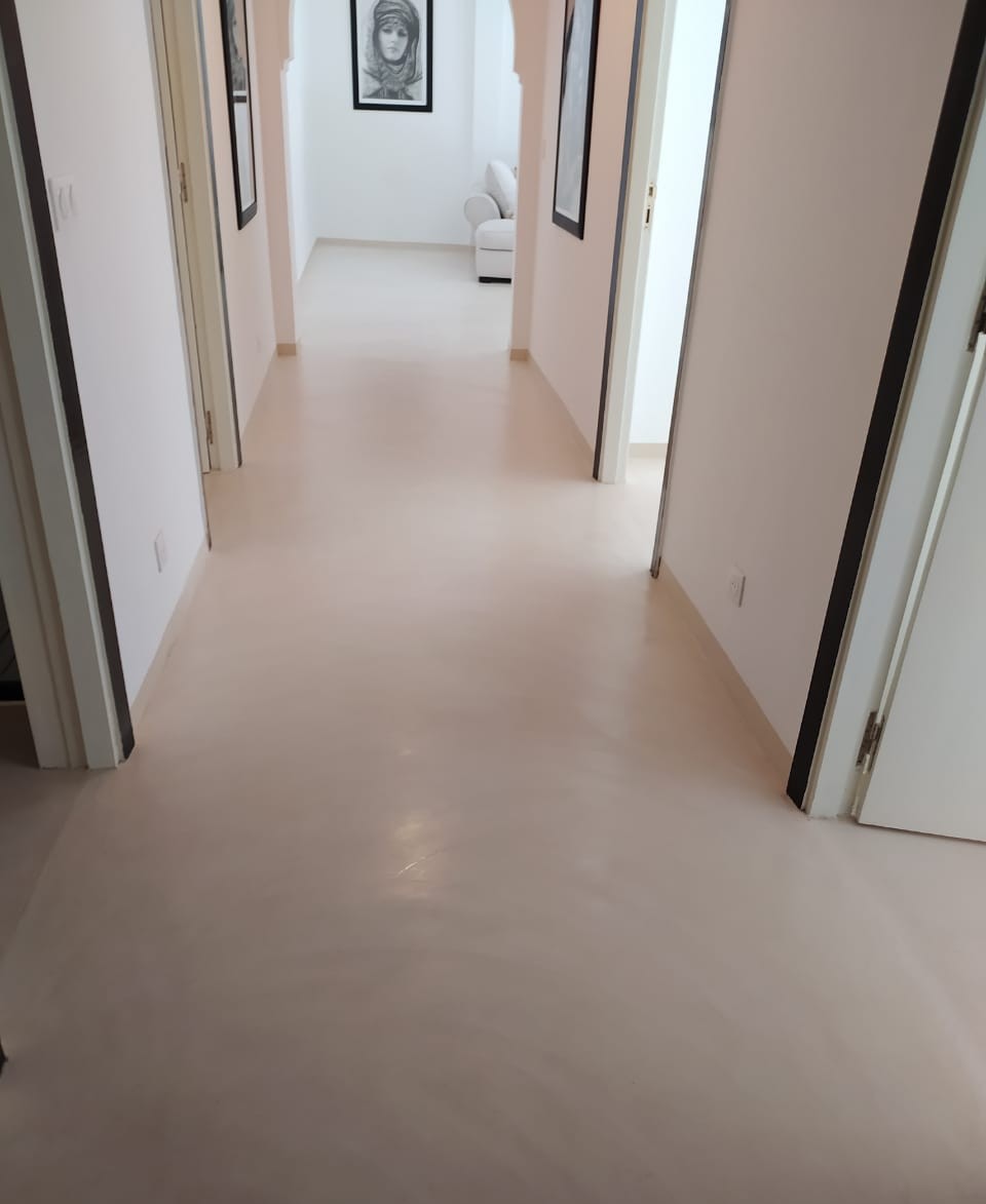 Un corridor moderne aux murs blancs, doté d’un sol en béton ciré lisse et brillant, et de cadres minimalistes accrochés sur les murs pour une ambiance épurée