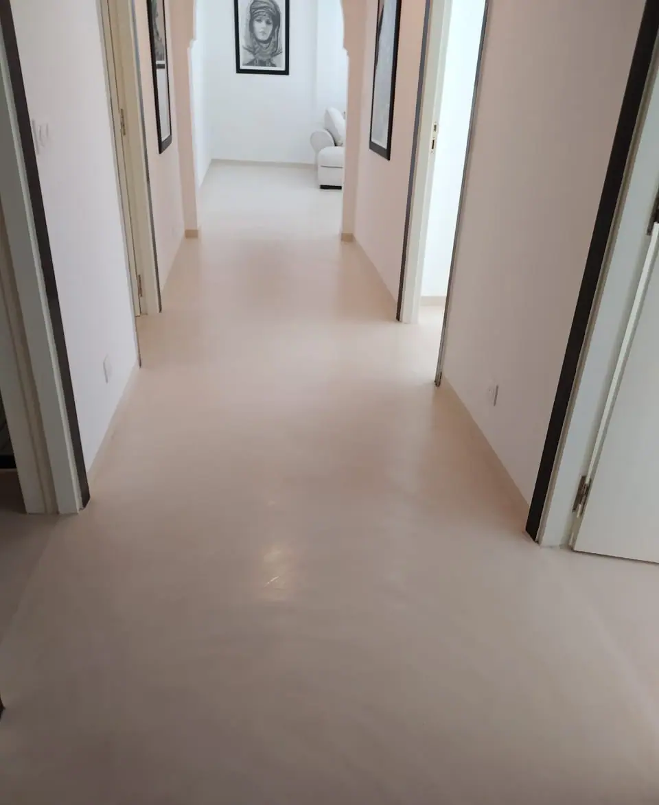 Un corridor moderne aux murs blancs, doté d’un sol en béton ciré lisse et brillant, et de cadres minimalistes accrochés sur les murs pour une ambiance épurée