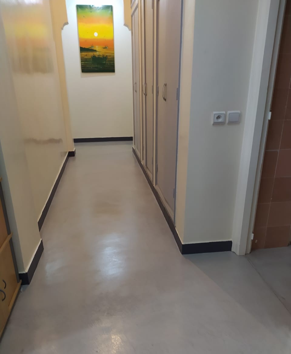 Un corridor moderne aux murs blancs, doté d’un sol en béton ciré blanc brillant et d’une peinture murale représentant un coucher de soleil pour une touche de couleur