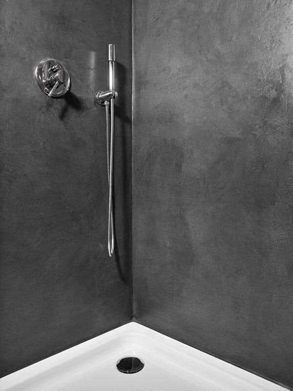 Douche moderne aux murs en béton ciré noir, dotée d’une robinetterie chromée et d’un pommeau de douche mural pour une ambiance raffinée.