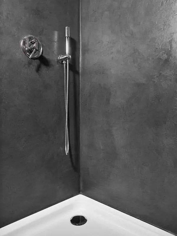 Douche moderne aux murs en béton ciré noir, dotée d’une robinetterie chromée et d’un pommeau de douche mural pour une ambiance raffinée.