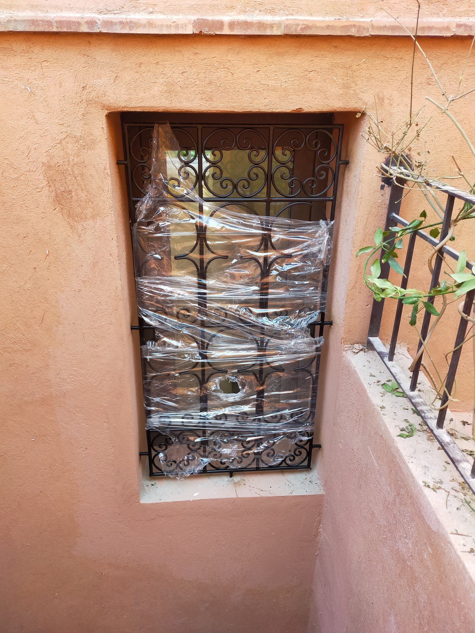 Fenêtre extérieure en maçonnerie rose, dotée d’une grille métallique ornée