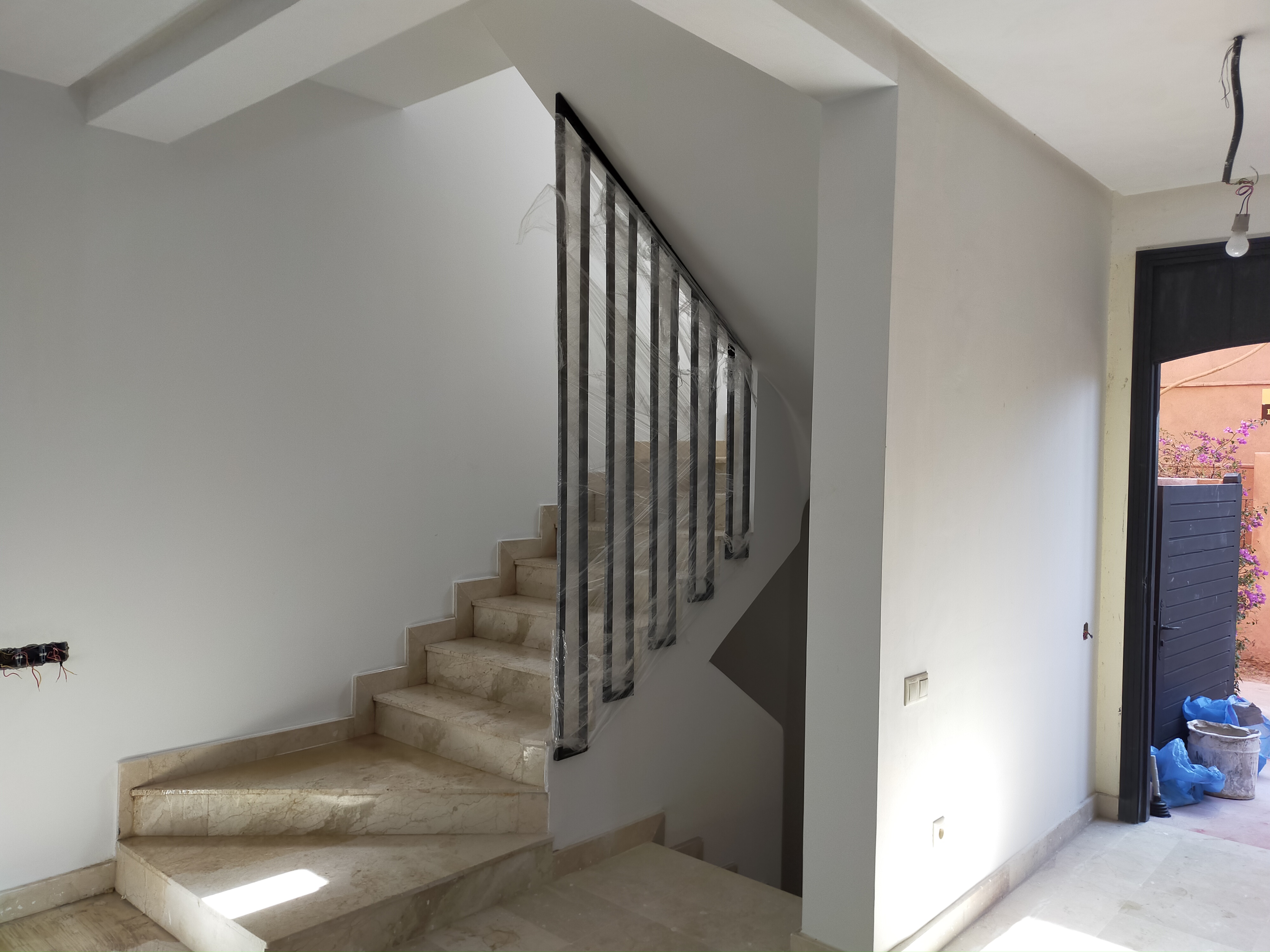 Escalier intérieur contemporain aux marches en marbre clair, doté d’une rampe métallique noire et de murs blancs pour une ambiance lumineuse