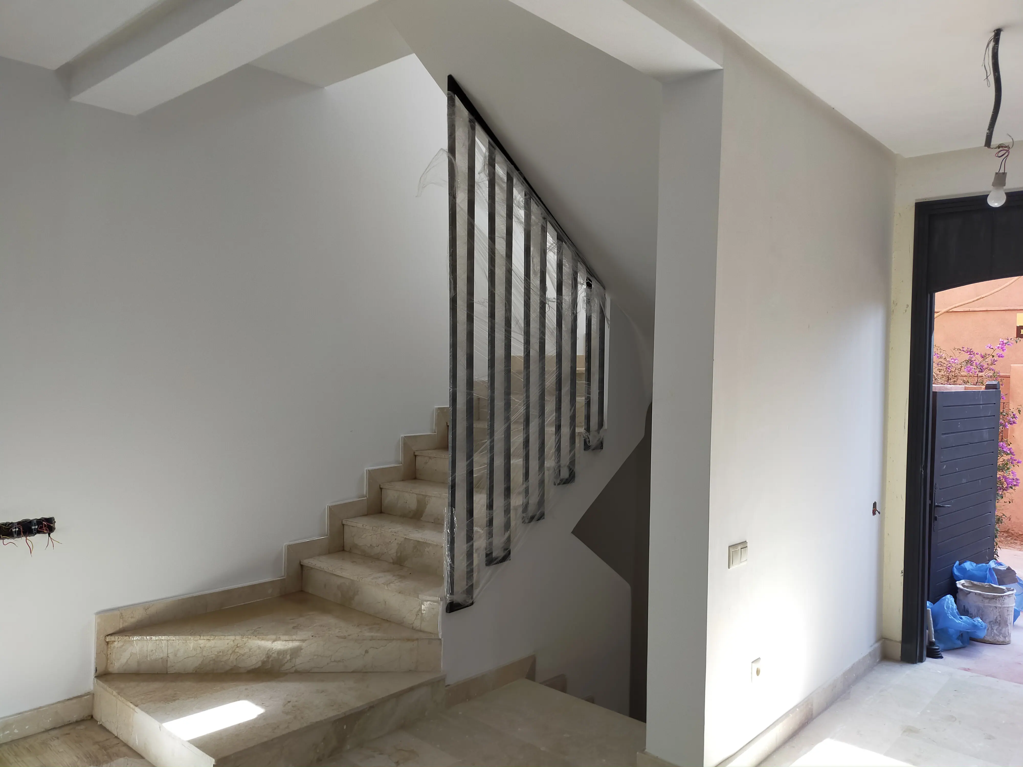 Escalier Moderne avec Rampe Métallique et Sol en Marbre Escalier intérieur contemporain aux marches en marbre clair, doté d’une rampe métallique noire et de murs blancs pour une ambiance lumineuse