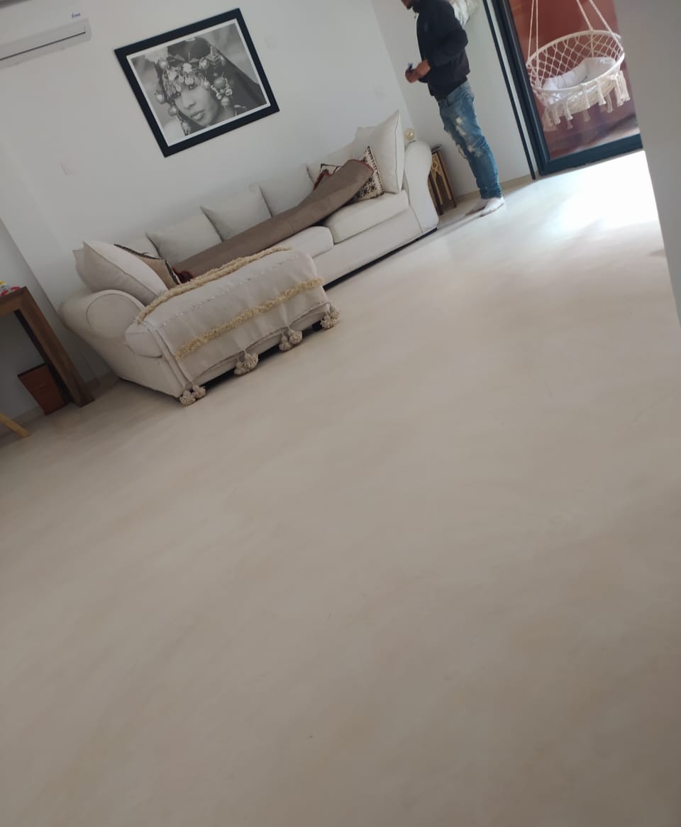 Séjour moderne aux murs blancs, doté d’un canapé blanc confortable, de coussins décoratifs, d’une peinture murale noire et blanche, et d’un sol en béton ciré pour une ambiance élégante